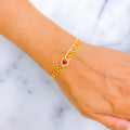 Gold bracelet with a red heart charm on a wrist against a marble background