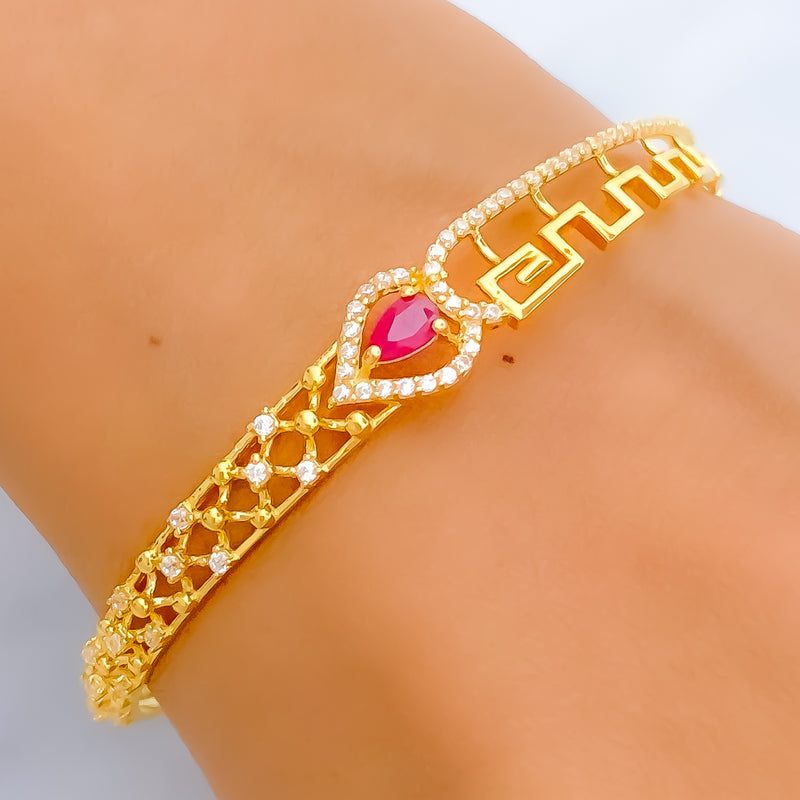 Gold bracelet with a red gemstone on a wrist against a neutral background