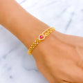 Gold bracelet with a red gemstone on a wrist against a marble background