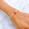 Gold bracelet with a pink peacock on a wrist against a marble background